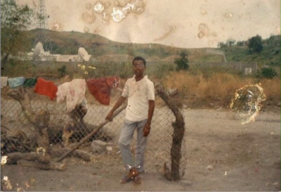 Apl at 14 in Pampanga, standing by a chain-link fence with laundry drying and hills behind.